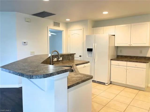Kitchen with white appliances, dark countertops, white cabinets, recessed lighting, and a peninsula