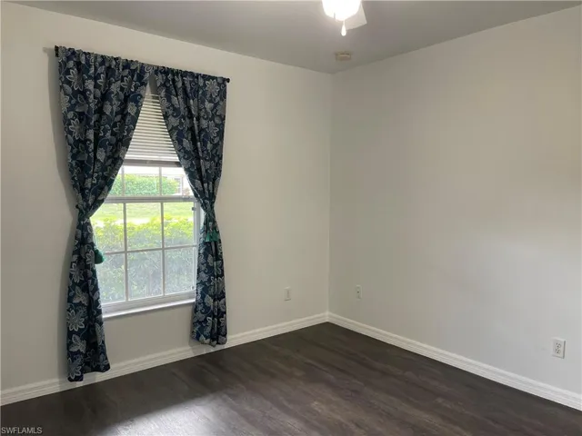 Empty room with dark wood-style flooring, a ceiling fan, and a smoke detector
