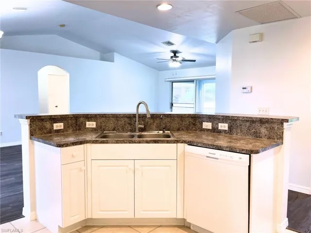 Kitchen with dishwasher, a ceiling fan, dark countertops, vaulted ceiling, and white cabinets