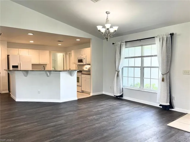 Kitchen with white appliances, dark countertops, a chandelier, a kitchen bar, and wood finished floors