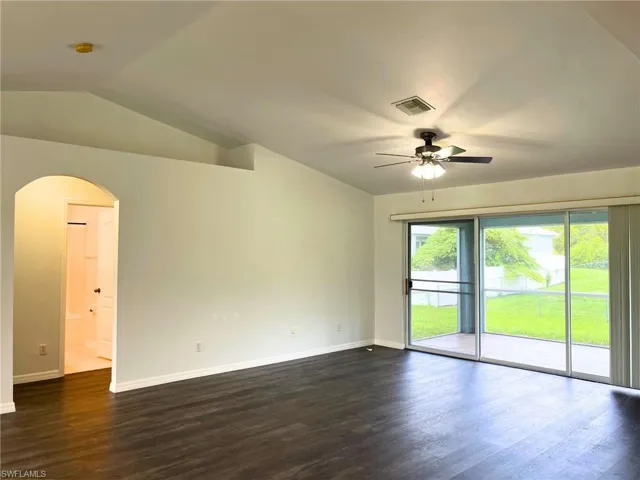 Empty room with ceiling fan, arched walkways, dark wood-type flooring, vaulted ceiling, and a smoke detector