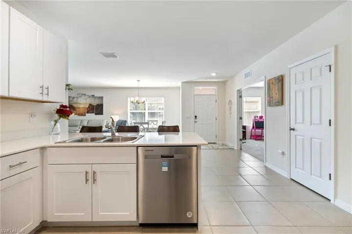 Kitchen featuring white cabinetry, stainless steel dishwasher, a chandelier, a peninsula, and light tile patterned floors