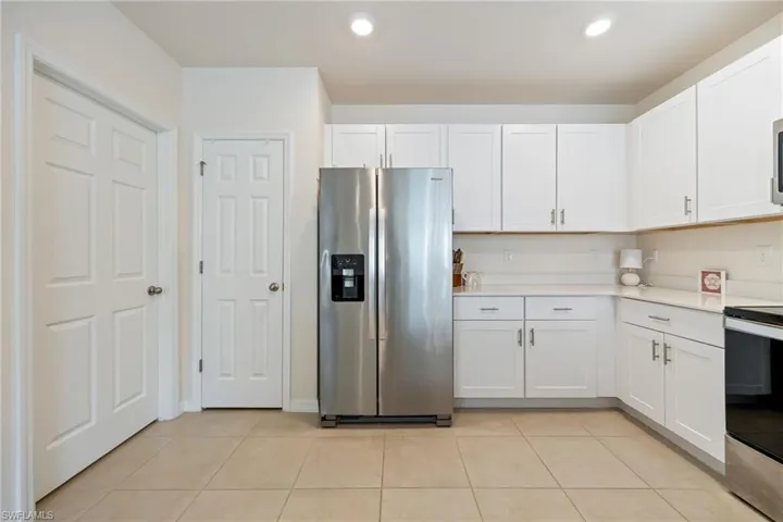 Kitchen featuring appliances with stainless steel finishes, white cabinets, light tile patterned floors, recessed lighting, and light stone counters