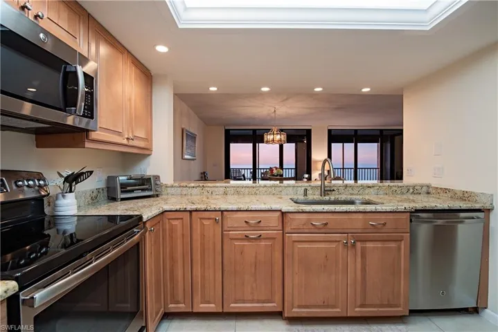 Kitchen with light stone countertops, sink, stainless steel appliances, kitchen peninsula, and a chandelier