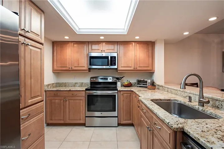 Kitchen with light stone countertops, a skylight, stainless steel appliances, sink, and light tile patterned flooring