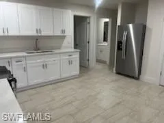 Kitchen with stainless steel fridge, white cabinetry, black stove, and sink