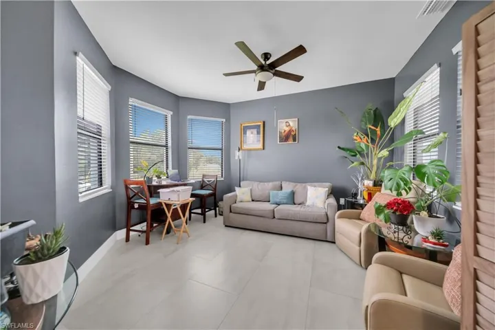 Spacious interior room featuring multiple windows with blinds, a ceiling fan, and light-toned tile flooring