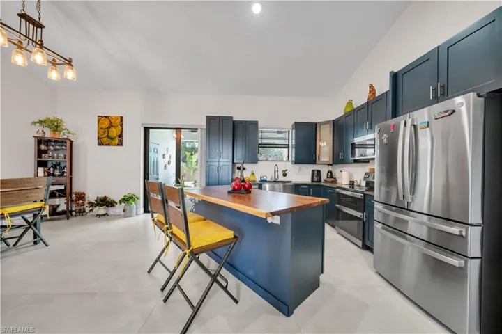 Kitchen featuring a central island with a wood-finish countertop, dark blue cabinetry, stainless steel appliances, and a vaulted ceiling