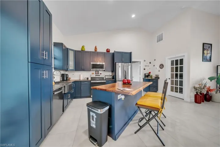 Kitchen featuring blue shaker-style cabinetry, stainless steel appliances, a wood butcher block island, and light-toned tile flooring