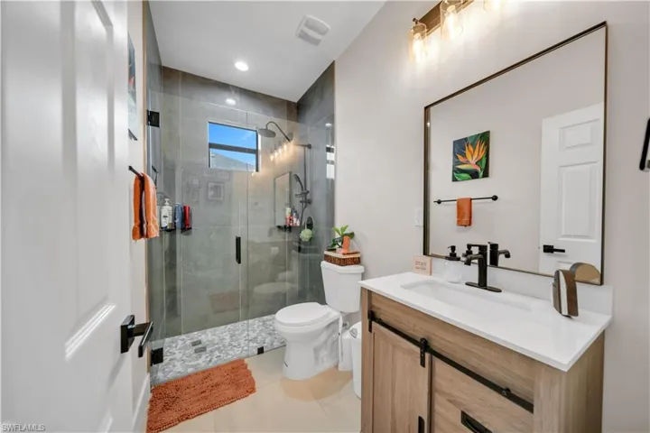 Bathroom featuring a frameless glass shower enclosure with gray tile surround, pebble flooring, and a window
