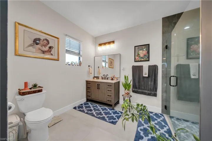 Contemporary bathroom featuring a glass-enclosed shower with dark stone-look tile, a single vanity with wood-finish cabinetry and a stone-look countertop, a rectangular mirror, and light-colored flooring