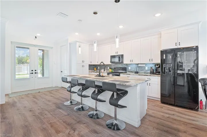 Kitchen featuring black appliances, light wood-type flooring, ornamental molding, light stone countertops, and french doors