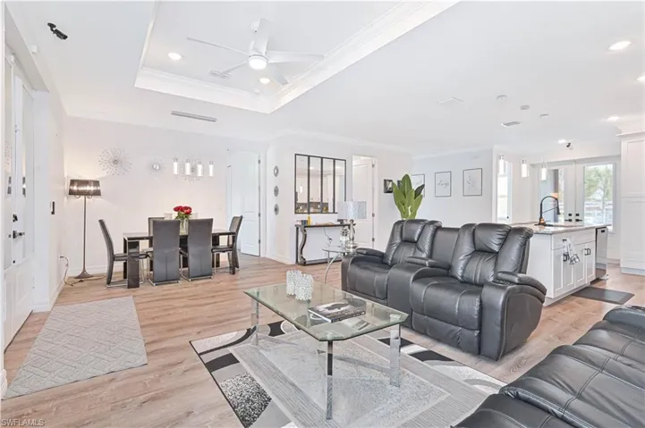 Living room with ornamental molding, light wood finished floors, a ceiling fan, a tray ceiling, and recessed lighting