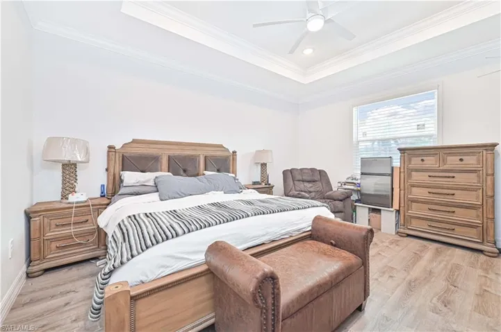 Bedroom featuring light wood-style flooring, ornamental molding, a tray ceiling, a ceiling fan, and recessed lighting