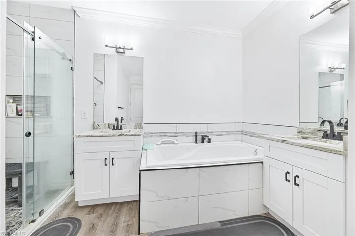 Bathroom featuring crown molding, a shower stall, a bath, two vanities, and wood finished floors