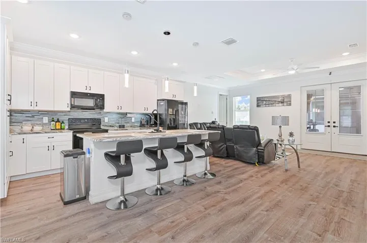Kitchen with ornamental molding, open floor plan, black appliances, a kitchen island with sink, and white cabinetry