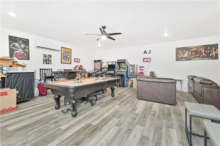 Recreation room with wood finished floors, ceiling fan, pool table, and a wall unit AC