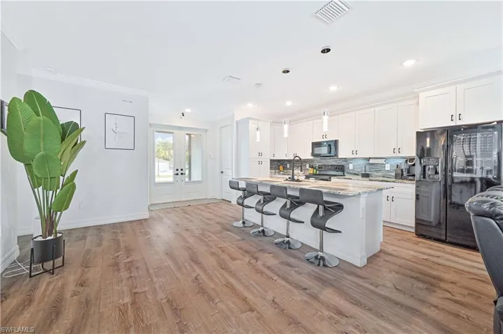 Kitchen featuring black appliances, ornamental molding, a breakfast bar, white cabinetry, and light wood finished floors