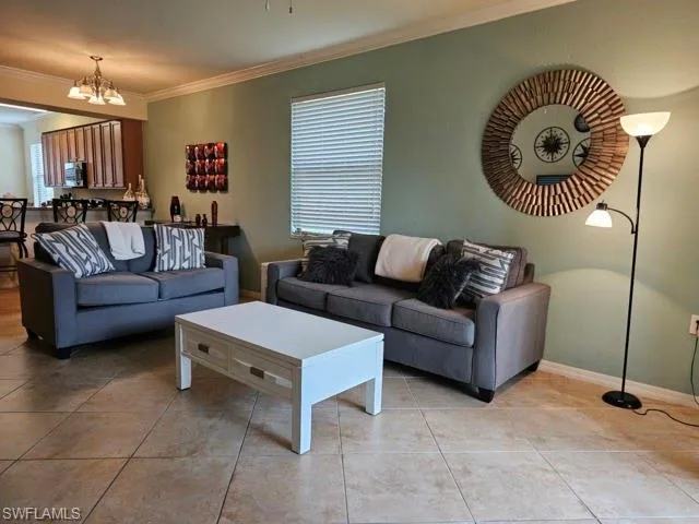 Living room with light tile patterned floors, baseboards, ornamental molding, and a chandelier