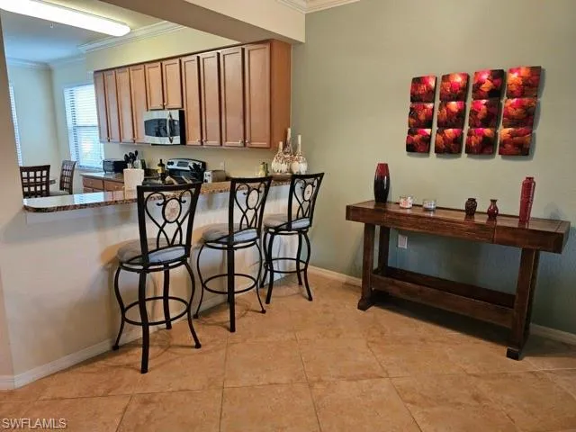 Kitchen with baseboards, brown cabinetry, ornamental molding, stainless steel appliances, and stone counters