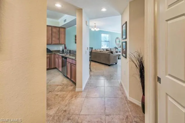 Kitchen featuring light tile patterned floors, stainless steel dishwasher, an inviting chandelier, brown cabinetry, and open floor plan
