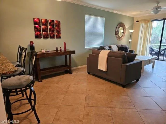 Living area with ornamental molding, light tile patterned flooring, baseboards, and a ceiling fan