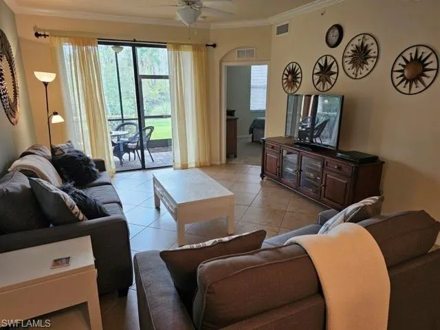 Living area with light tile patterned floors, ceiling fan, ornamental molding, and visible vents