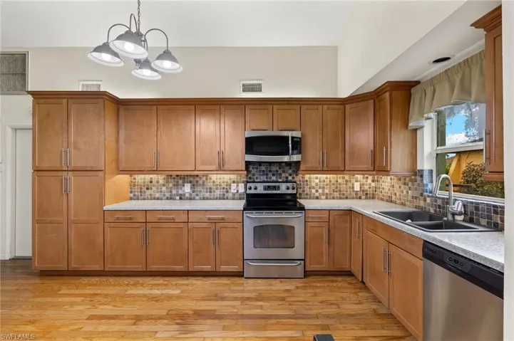 Kitchen with decorative backsplash, pendant lighting, light hardwood / wood-style flooring, and appliances with stainless steel finishes