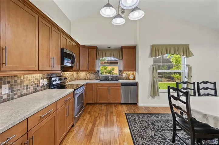 Kitchen with appliances with stainless steel finishes, tasteful backsplash, decorative light fixtures, light wood-type flooring, and a notable chandelier