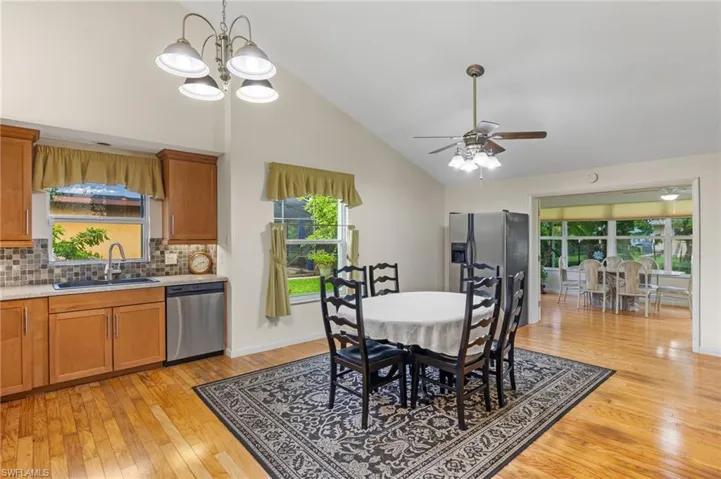 Dining room with light hardwood / wood-style floors, sink, ceiling fan with notable chandelier, and high vaulted ceiling