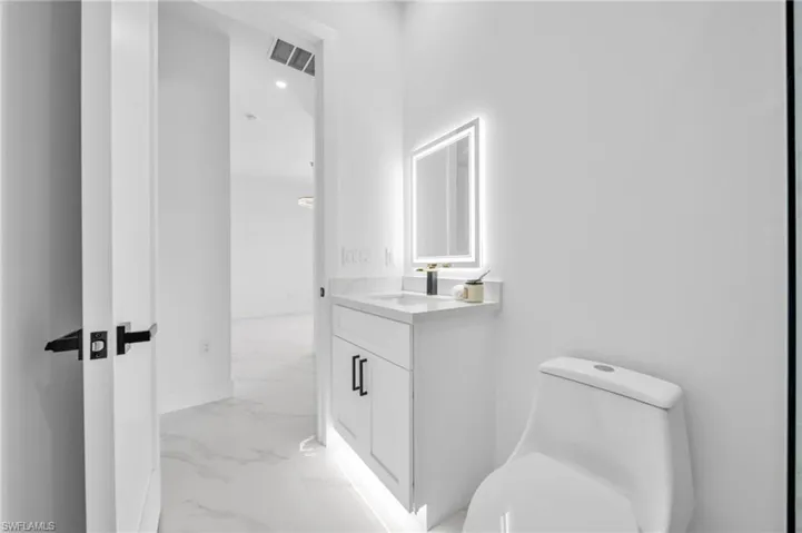 Half bath featuring marble look tiles, toilet, baseboards, and vanity