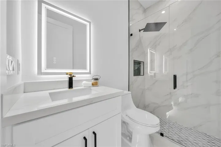 Bathroom with toilet, a marble finish shower, and vanity