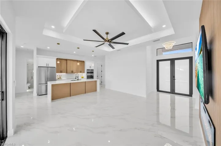 Kitchen with stainless steel fridge, a tray ceiling, open floor plan, light marble finish flooring, and light countertops