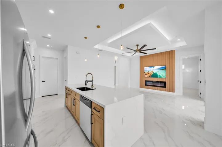 Kitchen with appliances with stainless steel finishes, a sink, a raised ceiling, a center island with sink, and recessed lighting