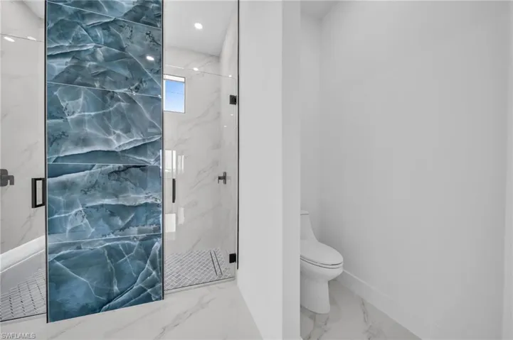 Full bath featuring toilet, a marble finish shower, marble finish flooring, and baseboards