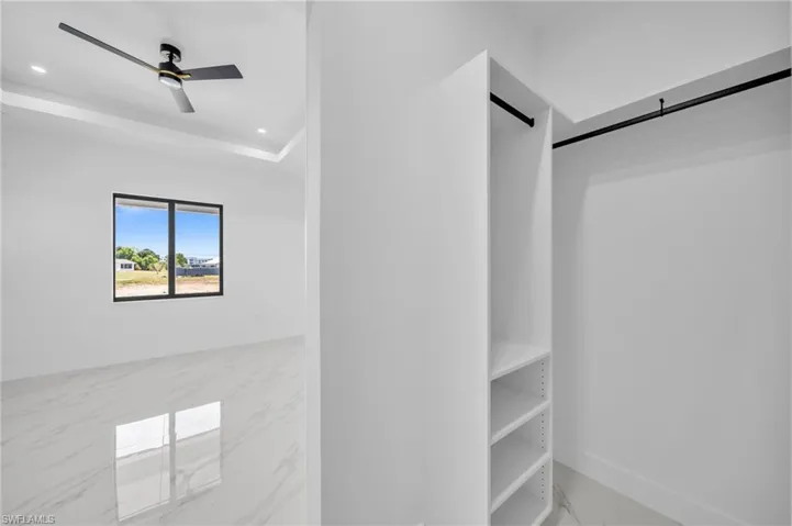 Spacious closet with a ceiling fan, a barn door, and marble finish floors