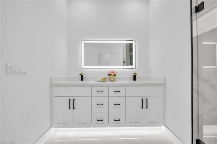 Full bathroom featuring baseboards, double vanity, marble finish flooring, and a marble finish shower