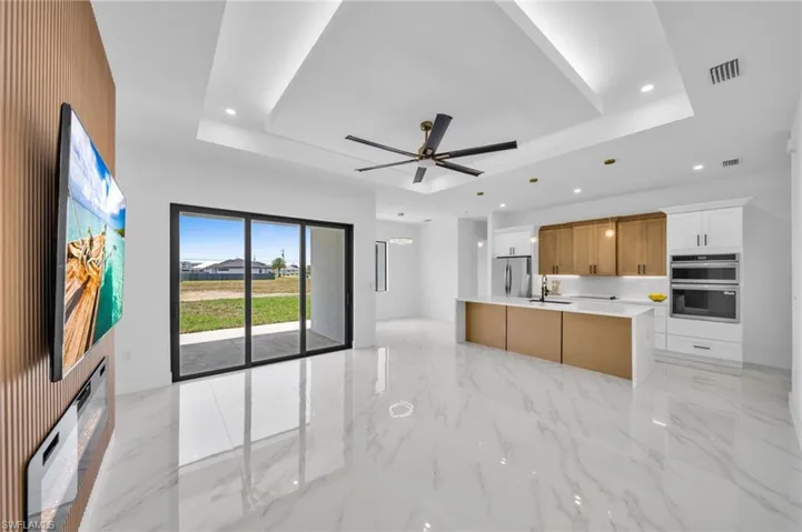 Kitchen with stainless steel appliances, a tray ceiling, ceiling fan, light countertops, and recessed lighting