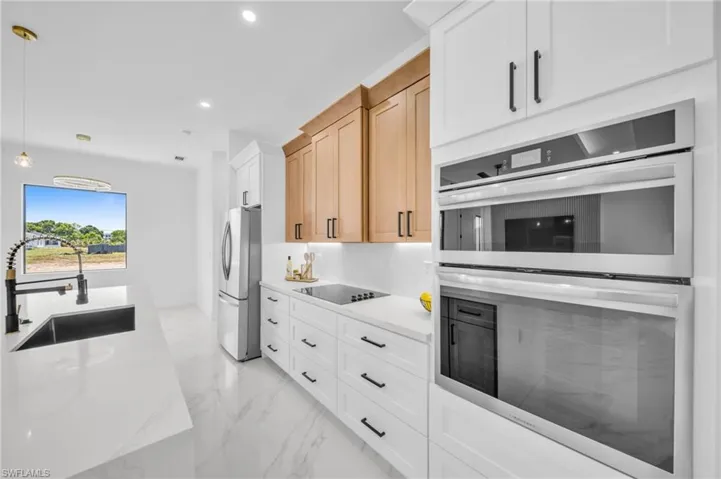 Kitchen featuring a sink, appliances with stainless steel finishes, light marble finish flooring, pendant lighting, and recessed lighting