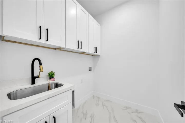 Laundry room featuring washer hookup, cabinet space, baseboards, and light marble finish flooring