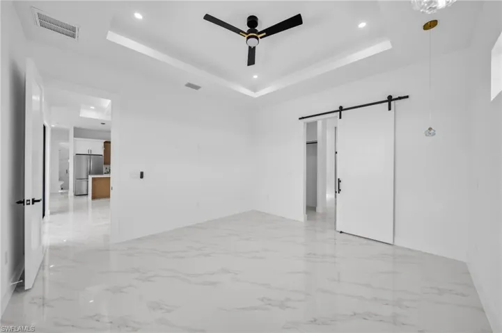 Empty room with a ceiling fan, a raised ceiling, a barn door, light marble finish flooring, and recessed lighting
