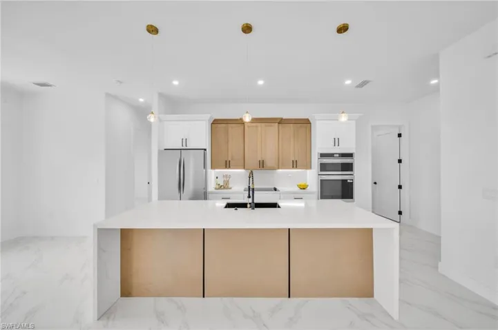Kitchen featuring stainless steel appliances, light marble finish flooring, a sink, an island with sink, and recessed lighting