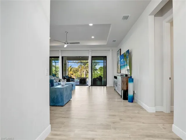 Living room featuring a raised ceiling, ceiling fan, and light wood-type flooring