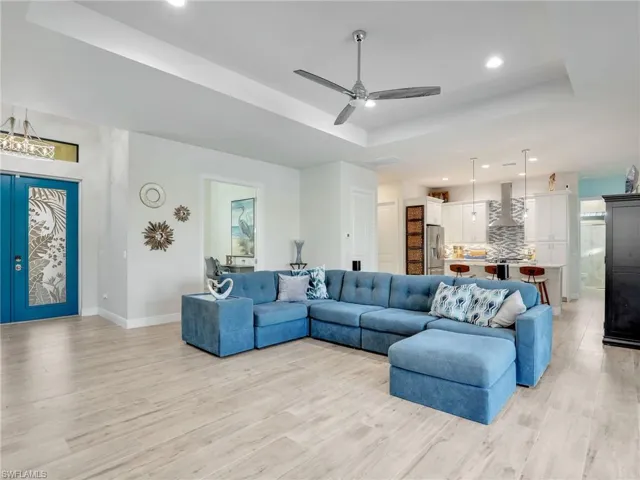 Living room featuring a raised ceiling, ceiling fan, and light wood-type flooring