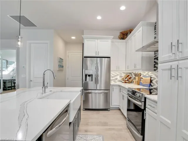Kitchen with stainless steel appliances, hanging light fixtures, white cabinets, and decorative backsplash