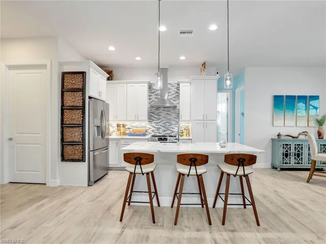Kitchen with pendant lighting, white cabinetry, stainless steel appliances, a center island with sink, and wall chimney range hood