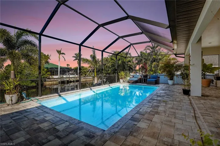 Pool at dusk featuring a water view, a patio area, and glass enclosure