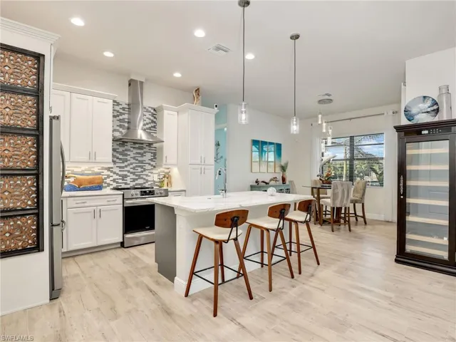 Kitchen featuring stainless steel appliances, a kitchen island with sink, wall chimney range hood, and white cabinets