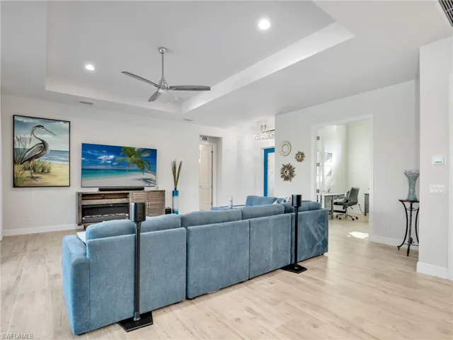 Living room with a raised ceiling, ceiling fan, a fireplace, and light hardwood / wood-style floors