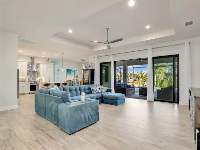 Living room with ceiling fan, a raised ceiling, and light hardwood / wood-style flooring
